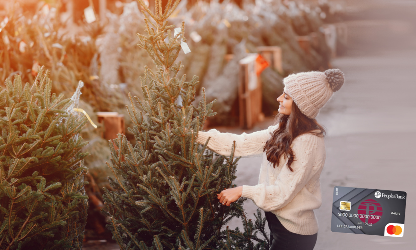 Woman picking out a Christmas tree with a Peoples Bank Mastercard Debit Card